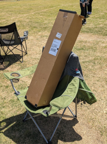 A cardboard box with black tape on the ends propped up in a folding chair.